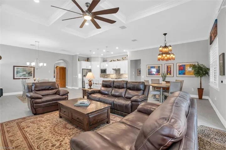 Living room with a chandelier, arched walkways, a ceiling fan, crown molding, and coffered ceiling