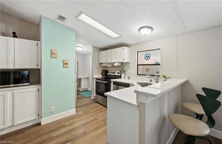 Kitchen with a breakfast bar, sink, white cabinets, kitchen peninsula, and stainless steel appliances