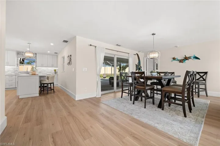 Crisp, bright, and effortlessly modern, the dining room invites conversation beneath a statement light fixture with views that stretch to the pool and greenscape beyond.