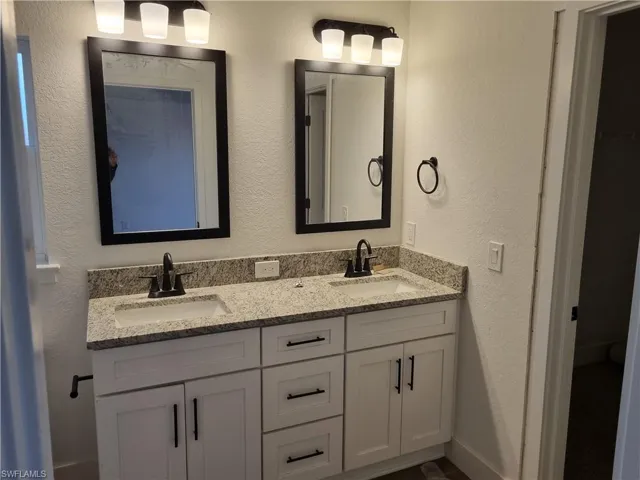 Full bathroom featuring a textured wall and double vanity