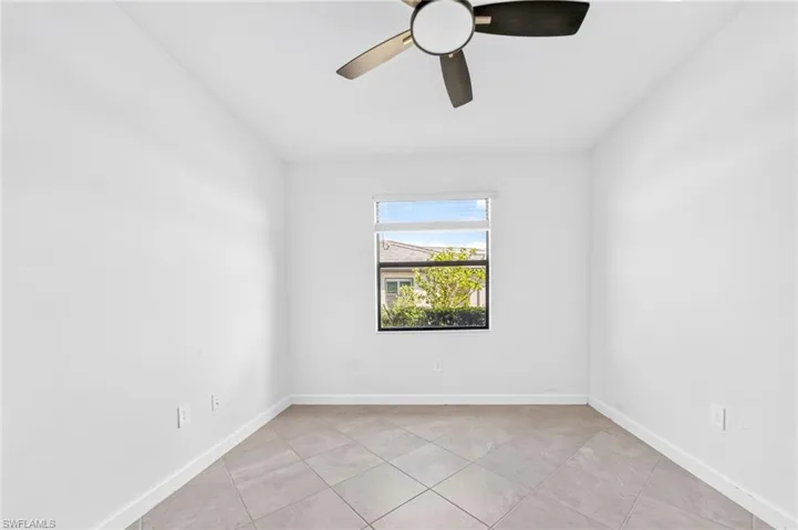 Room featuring neutral tile flooring, white wall finishes, a single-hung window with horizontal blinds, and a multi-blade ceiling fan with integrated lighting