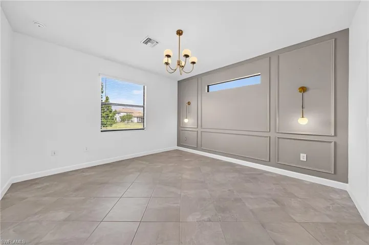 Room featuring large-format neutral tile flooring, an accent wall with decorative molding, a high horizontal transom window, a multi-globe chandelier, and dual wall-mounted pendant lights