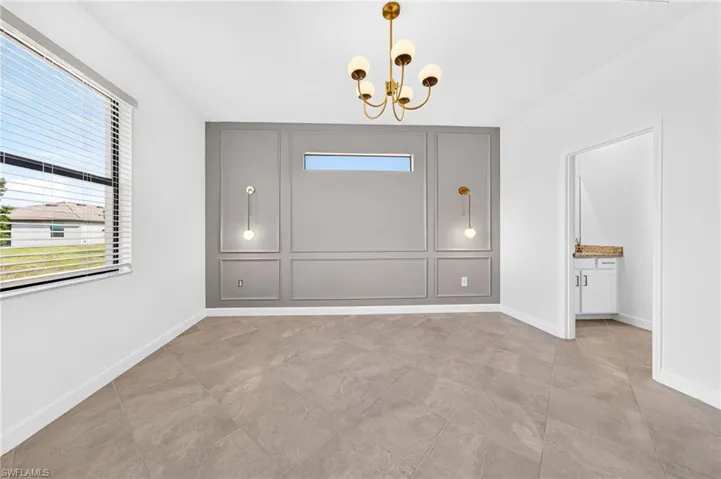 Room featuring tile flooring, accent wall with decorative molding, horizontal transom window, and brass-finish multi-arm chandelier and wall-mounted light fixtures
