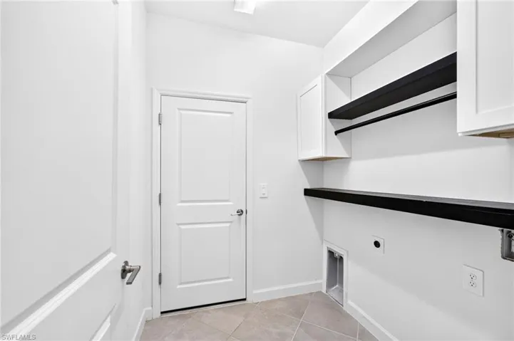 Utility area featuring white shaker-style wall cabinetry, integrated dark shelving, and tile flooring