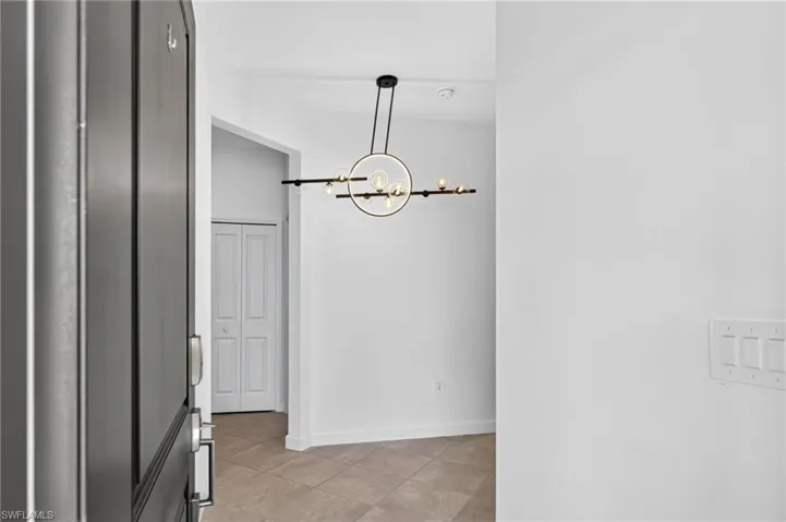 Foyer featuring tile flooring, a dark-toned entry door with a metal handle set, a modern multi-light chandelier with a matte black frame, and a white bifold closet door