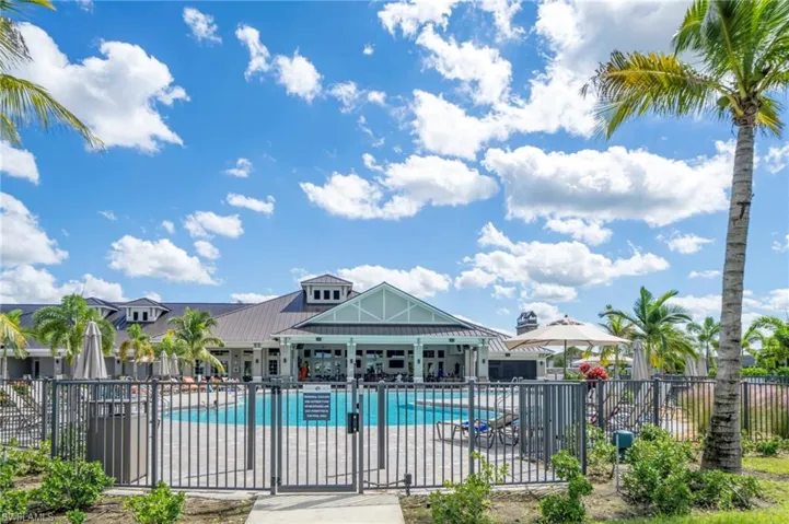 Community swimming pool with a brick-paver deck, metal fencing, and surrounding palm trees