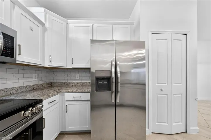 Kitchen featuring white shaker-style cabinetry, speckled stone-finish countertops, white subway tile backsplash, stainless steel appliances, and a bi-fold pantry door