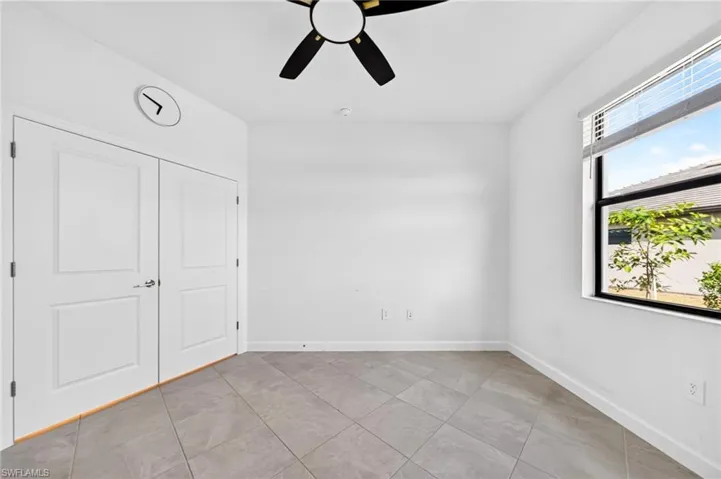 Room featuring neutral tile flooring, dual-panel closet doors, a multi-blade ceiling fan with integrated lighting, and a window with horizontal blinds