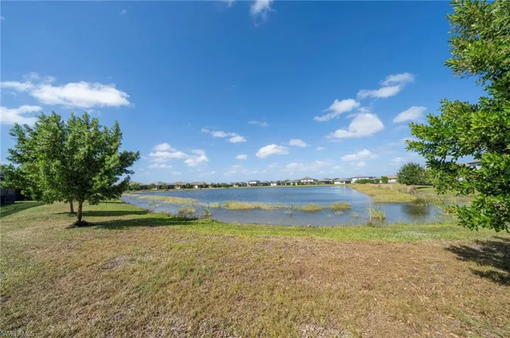Waterfront property featuring a retention pond, grassy grounds, and mature trees