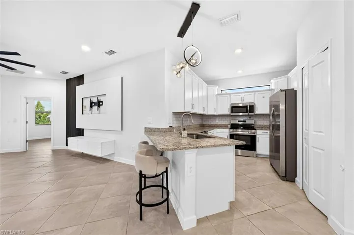 Kitchen featuring white cabinetry, stone-finish countertops, stainless steel appliances, a breakfast bar, and tile flooring