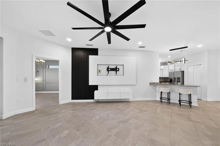 Large-format tile flooring, matte black multi-blade ceiling fan, and a built-in media wall featuring a textured black accent panel and white floating cabinetry