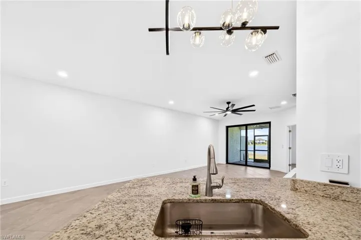 Stone countertop with an integrated stainless steel under-mount sink, multi-light contemporary chandelier, wood-finish flooring, ceiling fan with light fixture, and glass sliding doors