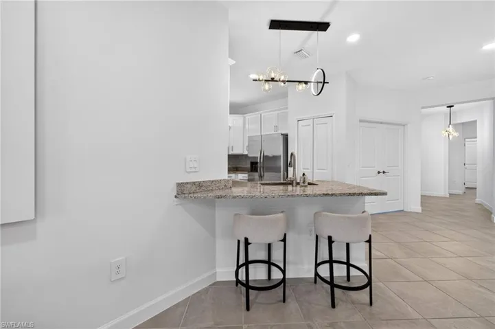 Kitchen peninsula featuring a stone-pattern countertop, stainless steel faucet, tile flooring, and a multi-globe linear pendant light fixture