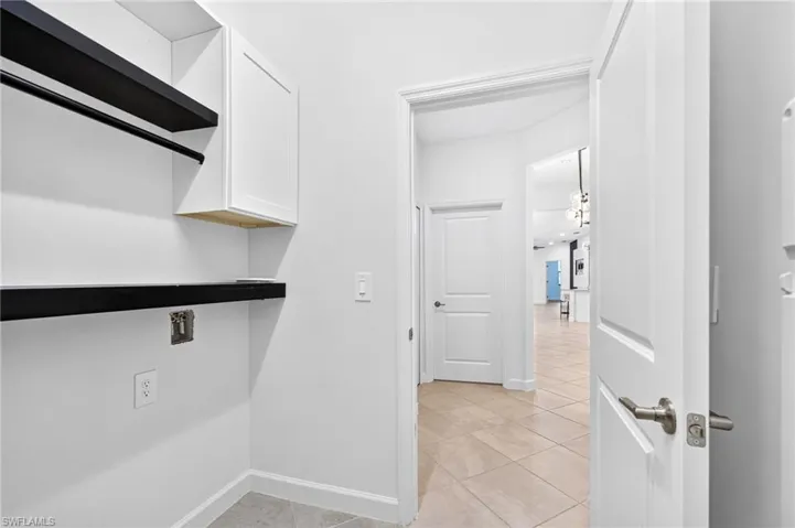Utility room featuring white shaker-style wall cabinetry, black open shelving, and tile flooring