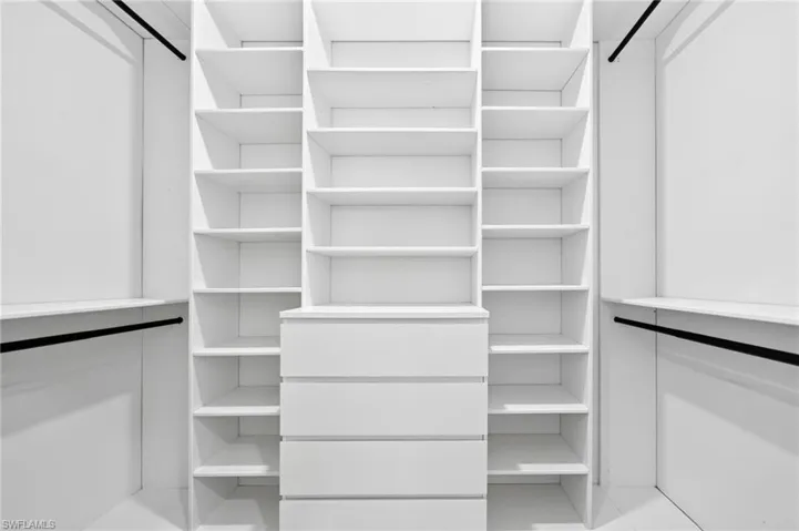 Custom walk-in closet featuring white built-in shelving, a central four-drawer dresser, and dual hanging rods