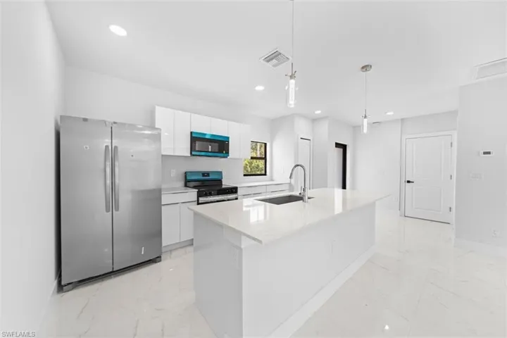 Contemporary kitchen featuring stainless steel side-by-side refrigerator, white cabinetry with integrated hardware, quartz waterfall island countertop, stainless steel sink with gooseneck faucet, and built-in stainless steel appliances