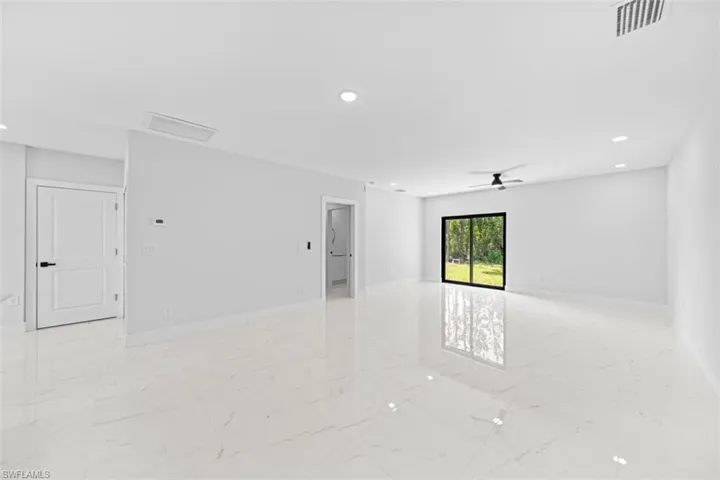 Spacious open-concept room featuring polished light-finish flooring throughout, recessed ceiling lighting, and abundant natural light from a large fixed window