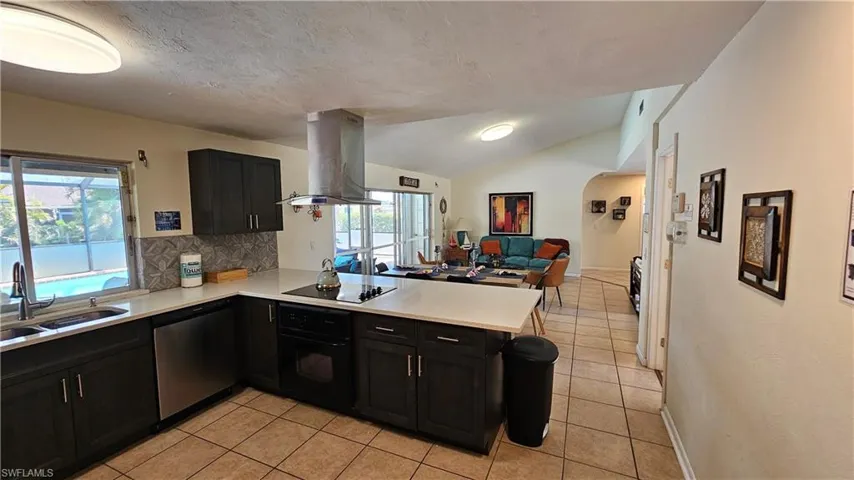Kitchen featuring sink, island range hood, vaulted ceiling, kitchen peninsula, and black appliances