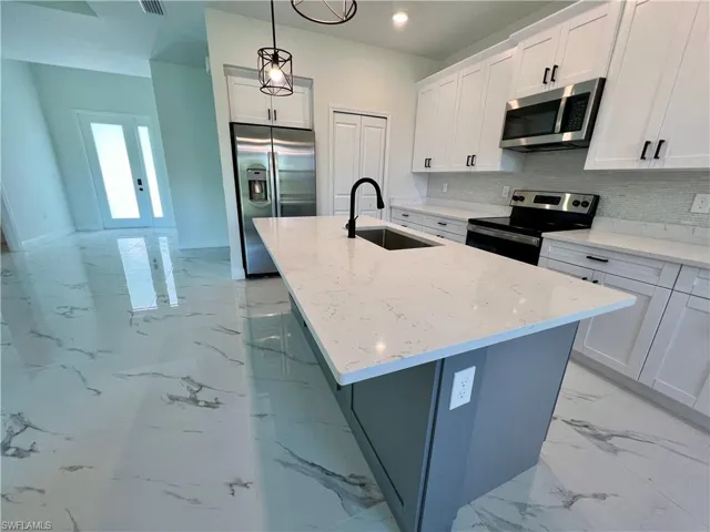 Kitchen featuring white cabinets, a center island with sink, appliances with stainless steel finishes, and sink