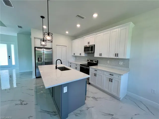 Kitchen featuring appliances with stainless steel finishes, a kitchen island with sink, sink, and white cabinetry