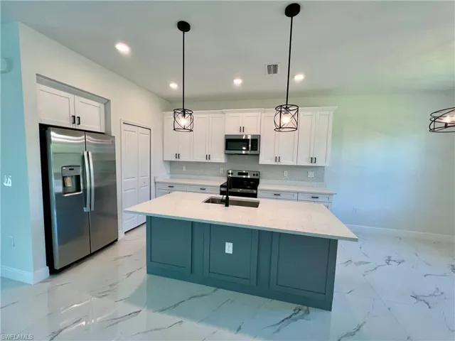 Kitchen with hanging light fixtures, sink, stainless steel appliances, and white cabinets