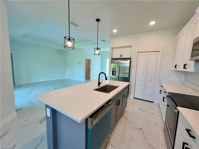 Kitchen featuring pendant lighting, sink, white cabinetry, stainless steel appliances, and a center island with sink