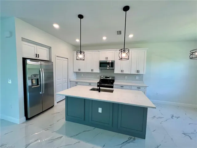 Kitchen featuring appliances with stainless steel finishes, white cabinets, pendant lighting, a center island with sink, and sink