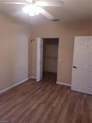 Unfurnished bedroom featuring wood finished floors, a ceiling fan, and a walk in closet