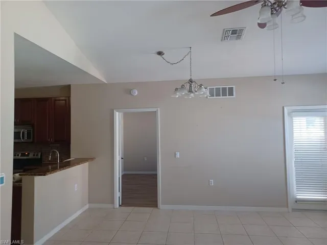 Kitchen with dark stone counters, light tile patterned floors, decorative light fixtures, stainless steel microwave, and a ceiling fan