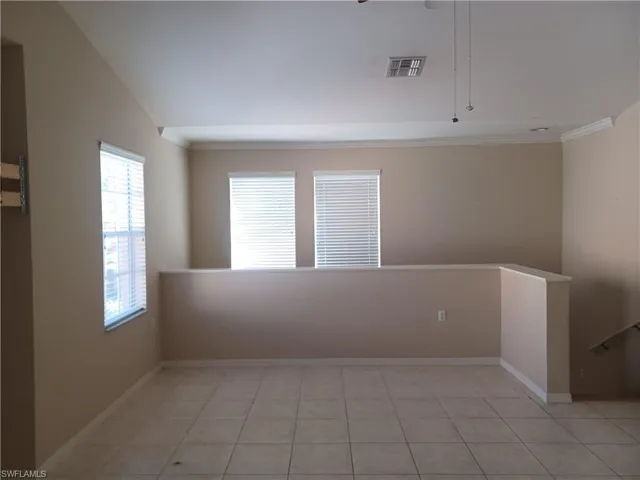 Unfurnished room featuring light tile patterned floors, crown molding, and lofted ceiling
