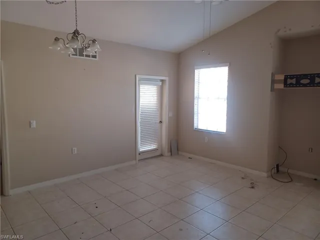 Empty room with vaulted ceiling, a chandelier, and light tile patterned flooring