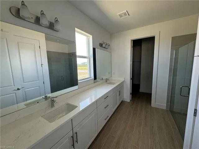 Primary bathroom with dual-sinks, walk-in shower, and large walk-in closet
