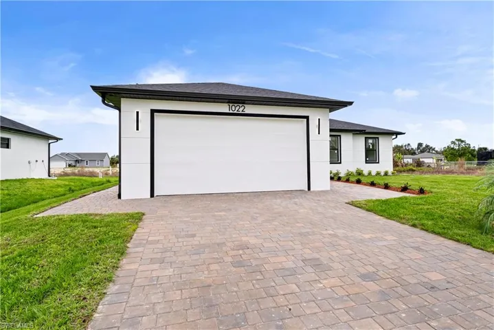 Prairie-style house featuring a front lawn, decorative driveway, stucco siding, and a garage