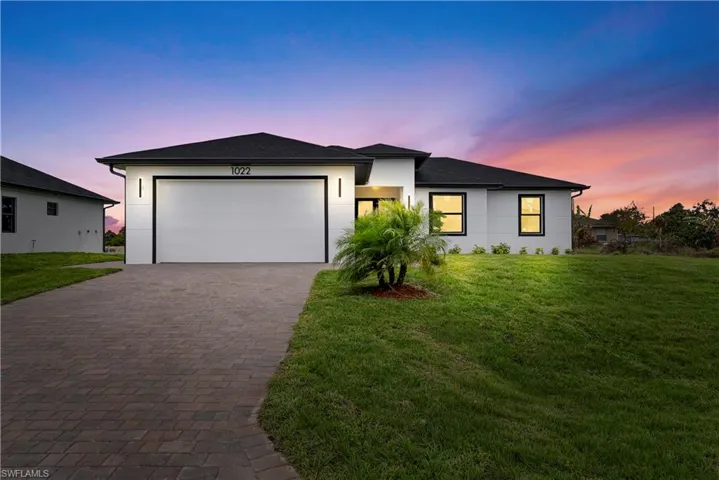 View of front facade featuring a lawn, a garage, driveway, stucco siding, and a shingled roof