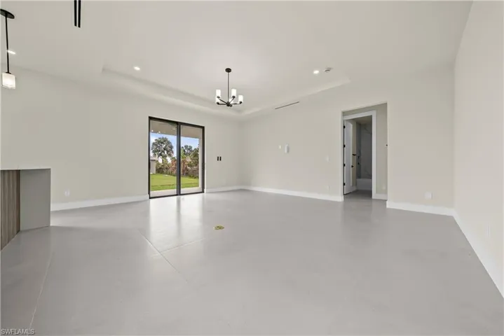 Empty room with concrete flooring, a chandelier, and a raised ceiling