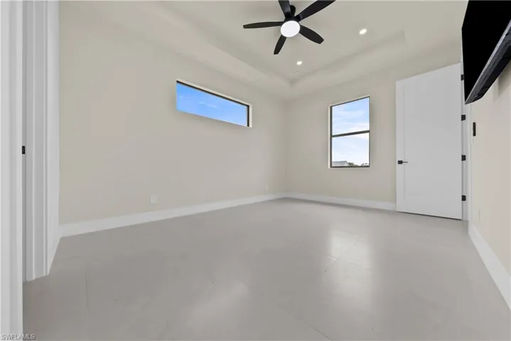 Empty room with finished concrete flooring, plenty of natural light, ceiling fan, a raised ceiling, and recessed lighting