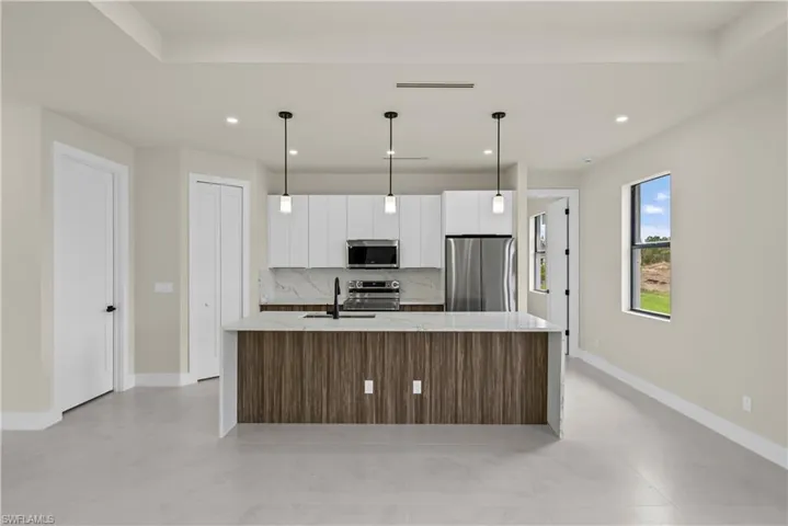 Kitchen with stainless steel appliances, modern cabinets, light stone countertops, a center island with sink, and hanging light fixtures