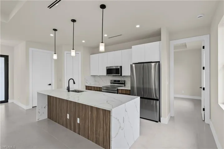 Kitchen with two tone cabinets, light stone counters, stainless steel appliances, modern cabinets, and pendant lighting