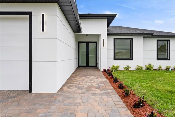Property entrance with a yard, stucco siding, and roof with shingles