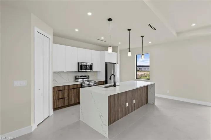 Kitchen featuring dual tone cabinets, stainless steel appliances, light stone countertops, a kitchen island with sink, and pendant lighting