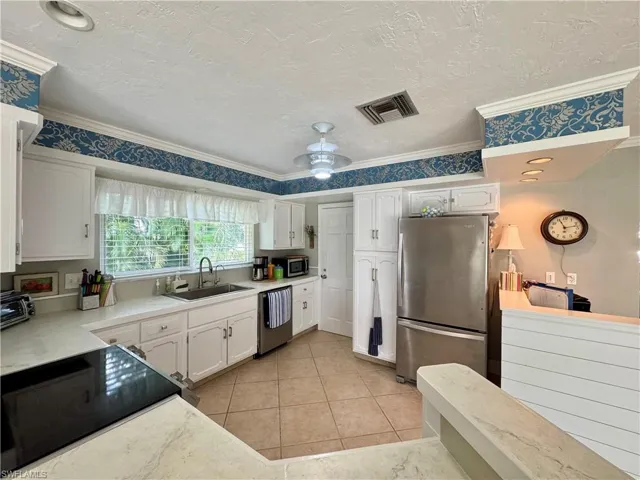 Kitchen featuring stainless steel appliances, light countertops, white cabinetry, a textured ceiling, and light tile patterned flooring