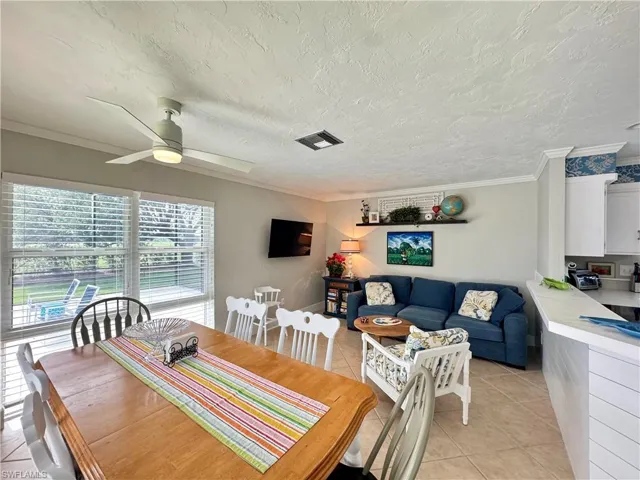 Dining area with ornamental molding, light tile patterned flooring, a textured ceiling, and a ceiling fan