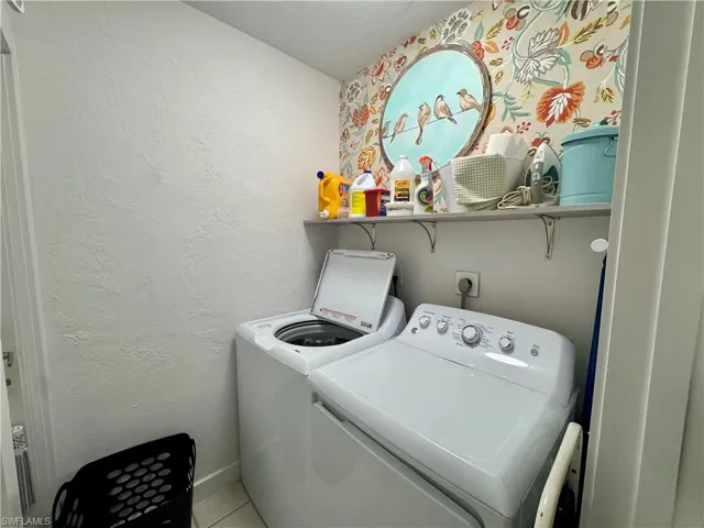 Laundry area with a textured wall, washing machine and clothes dryer, and tile patterned flooring