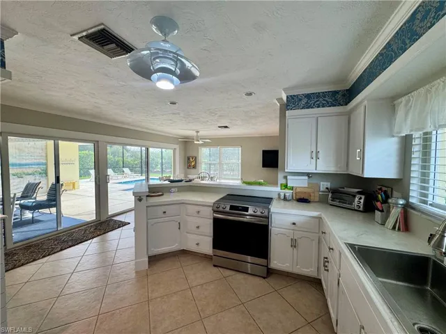 Kitchen with white cabinets, stainless steel range with electric stovetop, a peninsula, a textured ceiling, and light tile patterned floors