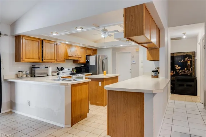 Kitchen with a peninsula, wood finish cabinetry, light countertops, ceiling fan, and coffered ceiling