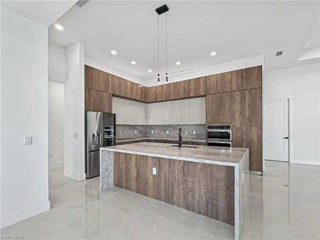 Kitchen featuring light stone counters, a large island, decorative backsplash, appliances with stainless steel finishes, and modern cabinets
