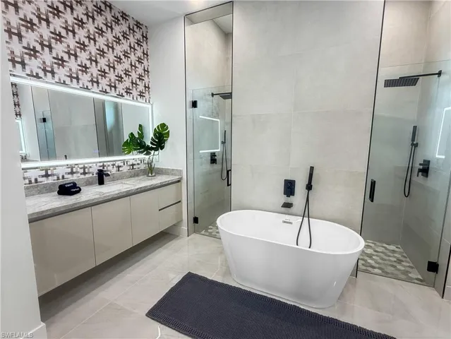 Spacious bathroom featuring a freestanding soaking tub, dual glass-enclosed shower, floating vanity with integrated sink, and an illuminated mirror