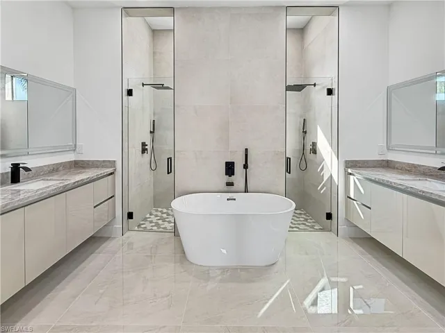 Bathroom with a freestanding bath, a shower stall, and two vanities