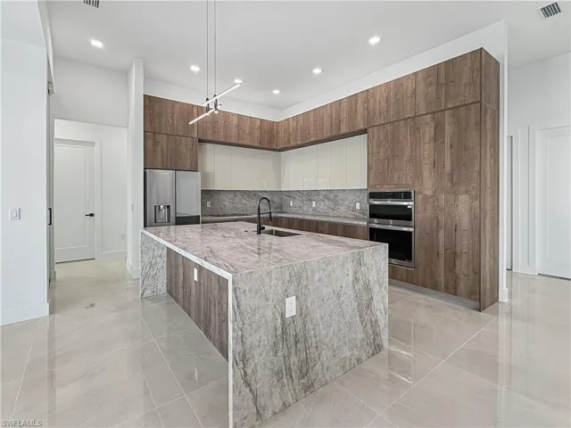 Kitchen with a center island with sink, modern cabinets, decorative backsplash, stainless steel appliances, and light stone counters