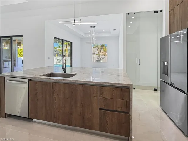 Kitchen with modern cabinets, appliances with stainless steel finishes, a tray ceiling, light stone countertops, and recessed lighting